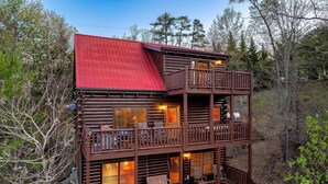 A multi-level cabin with a red roof, wooden balconies, and a pool area. - Buddy’s Mountain Hideaway (Sevierville)
