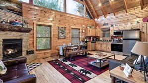 A cozy cabin interior with a fireplace, wooden walls, a dining area, and a kitchen. - Buddy’s Mountain Hideaway (Sevierville)