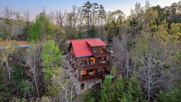 A multi-story wooden cabin with a red roof, surrounded by dense forest. - Buddy’s Mountain Hideaway (Sevierville)