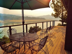 A deck with a round table and chairs, overlooking a body of water and distant hills. - Lakefront Chateaux with Dock, Unique Rock Wall for Privacy, and Internet (Lake Nacimiento)