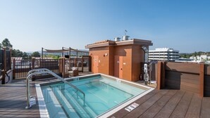 Zona de piscina en la azotea con vista despejada al horizonte urbano, una terraza de madera y una piscina con barandilla de seguridad.