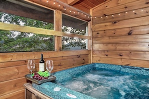 Une cabane en bois avec un bain à remous, une bouteille de vin et une assiette de raisins.