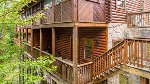 A log cabin with a wooden deck and multiple windows. - Heated Rst Pool-Dollywood-WIFI -Arcade-Parkway-Families-Shopping-Hot Tub-Shows (Pigeon Forge)