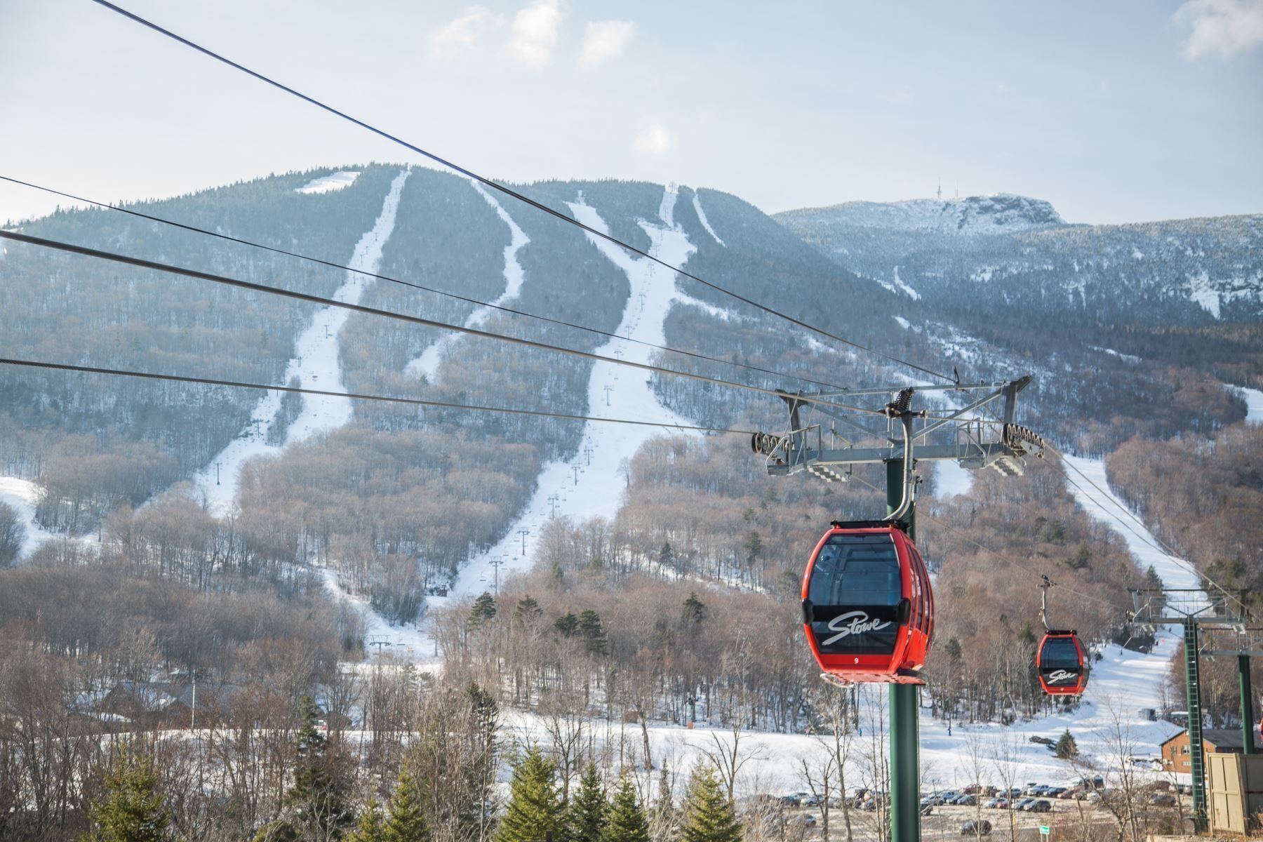 A ski lift with cabins, a snowy mountain backdrop, and a clear sky.