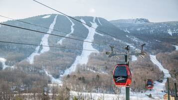 A ski lift with cabins, a snowy mountain backdrop, and a clear sky.