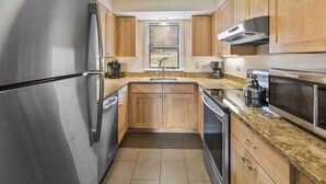 A compact kitchen with stainless steel appliances, wooden cabinets, and a window with blinds. - Condo at Stowe`s Toll House | Ski-in/Ski-out! (Stowe)