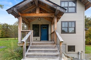 Stroll up to the charming entrance, featuring a wooden porch and stairs leading to a welcoming door.