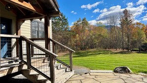 Une maison en bois avec un escalier en pierre menant à un porche, entourée d’une pelouse bien entretenue et d’arbres.