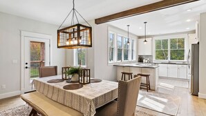 Une cuisine spacieuse dotée d’un îlot central, de grandes fenêtres et d’un coin repas avec une banquette et des chaises.
