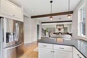 Enjoy cooking in this kitchen with a stainless steel refrigerator, white cabinetry, and a large window offering a view of the outdoors.