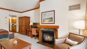 A living room with a fireplace, wooden furniture, and a view of the kitchen through an open door. - 2nd Floor Studio in The Lodge at Spruce Peak (Stowe)