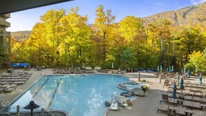A pool area with lounge chairs and a hot tub, surrounded by trees with autumn foliage. - 2nd Floor Studio in The Lodge at Spruce Peak (Stowe)