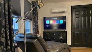 A modern living room with a reclining chair, a flat-screen TV, and a dark wooden door.