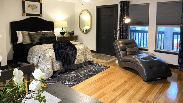A bedroom with a bed, a chair, a desk, a mirror, a ceiling fan, and a door.