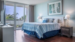 Une chambre à coucher comprenant un lit, des tables de chevet, un ventilateur de plafond et une vue sur l’extérieur, accessible par une porte-fenêtre coulissante.