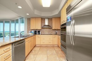 A modern kitchen with stainless steel appliances, wooden cabinets, and a large island with a sink. - Three Bedroom with Media Room with Wrap-Around Balcony. Complimentary Boat Slip! (Orange Beach)