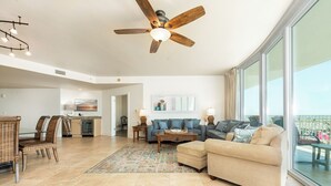 Ein großzügiges Wohnzimmer mit großem Fenster, Deckenventilator und Essbereich, im Hintergrund eine Küche.