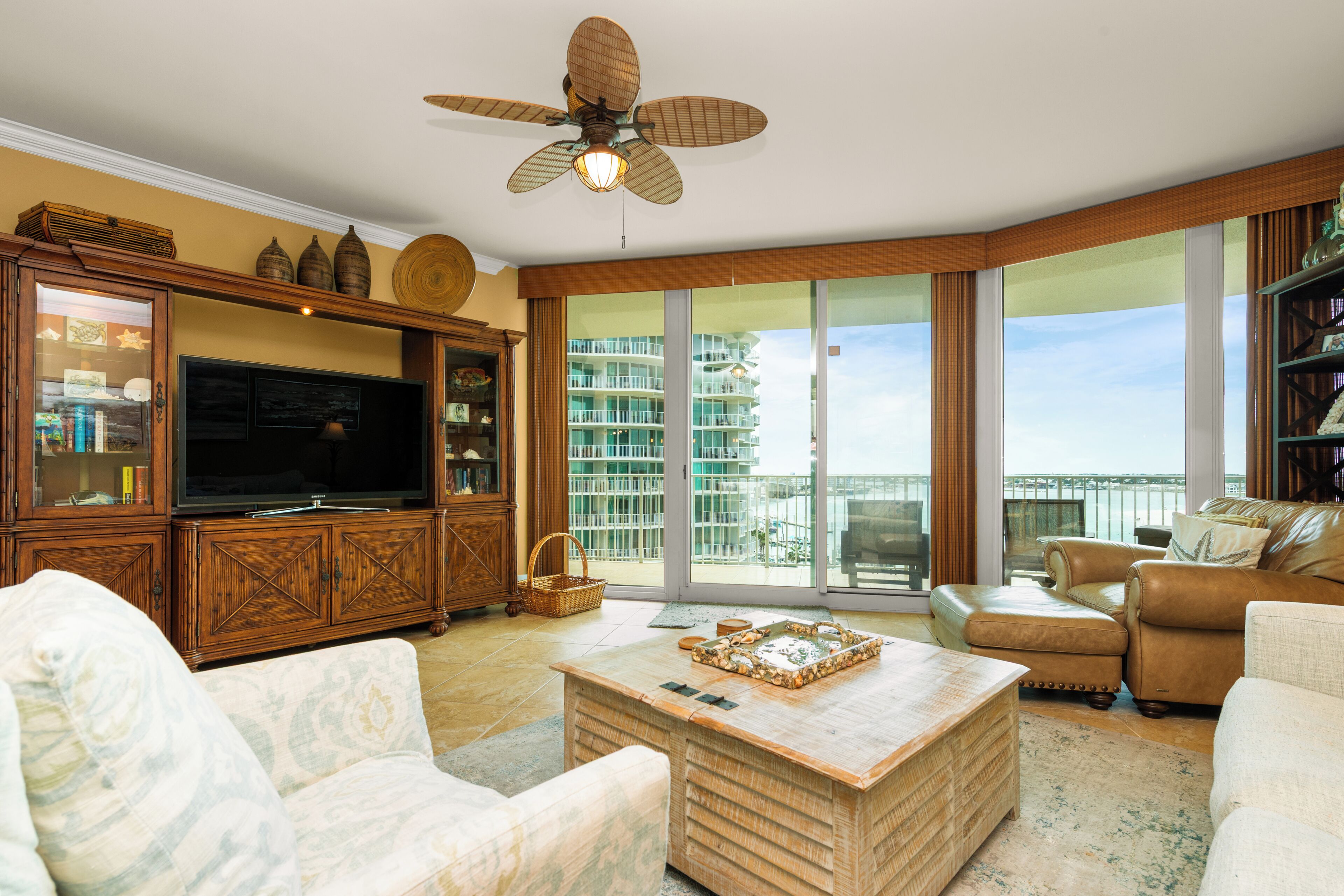 A living room with a television, a ceiling fan, and a large window with a view of a building.