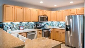 Una cocina con gabinetes de madera, un refrigerador de acero inoxidable, un microondas y un salpicadero de azulejos.