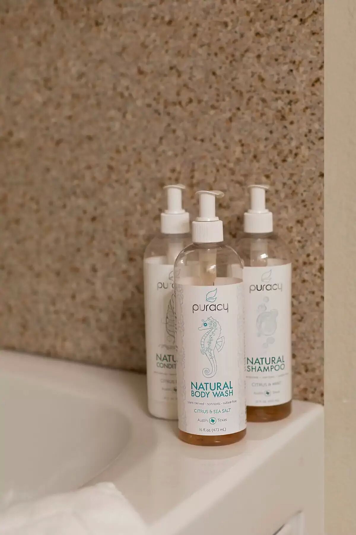 Três frascos de Puracy Natural Body Wash sobre uma pia de banheiro.