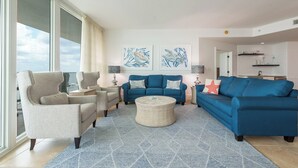 Amplia sala de estar con un ventanal grande, un sofá azul, un sillón color beige y una mesa de centro redonda.