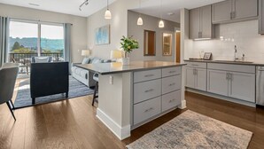 Una cocina moderna con gabinetes grises, una isla central, iluminación colgante y vistas amplias a través de grandes ventanales.