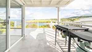 A balcony with a grill, glass doors, and a view of a lake and hills. - Kiama Home By the Sea, Beach and Mountain Views - Newly Renovated (Kiama)