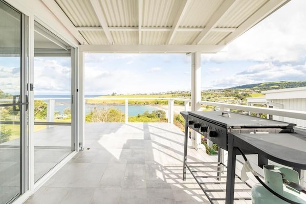 A balcony with a grill, glass doors, and a view of a lake and hills.