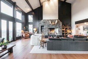 A spacious living room with a stone fireplace, large windows, and a view of the outdoors. - Incredible 8 Bedroom Aerie Estate - Minutes to Main Street - Unobstructed Views of Park City (Park City)