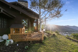 Uma casa de madeira com varanda, grandes janelas e vista para um vale e montanhas.