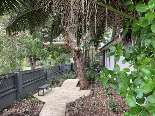 Stroll through the tranquil garden, surrounded by lush greenery and a variety of plants, to a shaded bench beneath a majestic tree.