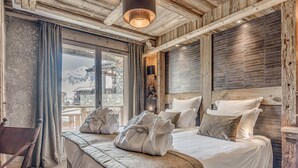 A spacious bedroom with a large bed, wooden headboard, and a view of a snowy mountain. - 5* Chalet in Tignes - 450m² - 16 guests - Sauna, Jacuzzi, Game Room (Tignes)