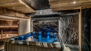 A modern spa area with a hot tub, wooden ceiling, and a stone wall. - 5* Chalet in Tignes - 450m² - 16 guests - Sauna, Jacuzzi, Game Room (Tignes)