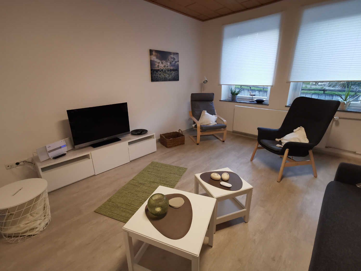 Un salon moderne doté d’un téléviseur à écran plat, de deux fauteuils, d’une petite table agrémentée d’objets décoratifs et d’une fenêtre avec des stores.