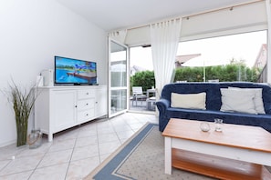 Ein modernes Wohnzimmer mit Fernseher, einer Couch, einem Couchtisch und einer Glastür, die auf eine Terrasse im Freien führt.