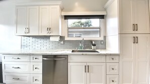 Una cocina con armarios blancos, lavavajillas de acero inoxidable y una ventana sobre el fregadero.