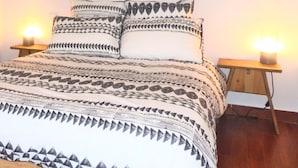 A bed with patterned bedding, two bedside lamps, and a window above the bed.