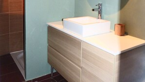 A modern bathroom with a white sink, a round mirror, and a wooden cabinet.