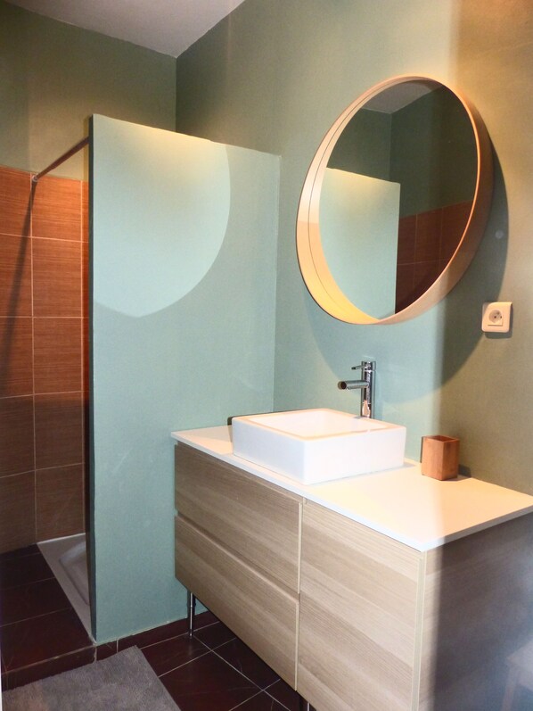 A modern bathroom with a white sink, a round mirror, and a wooden cabinet.