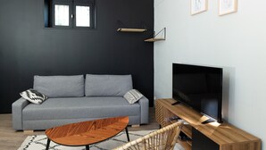 A modern living room with a grey sofa, a wooden coffee table, a flat-screen TV, and a black wall with minimal decor.