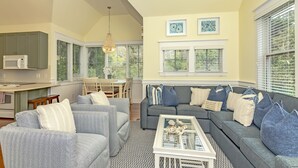 A modern living room with a gray sectional sofa, a coffee table, and a dining area with a white table and chairs. - Reverse floor plan cottage with screened in porch. Nature views! (Bald Head Island)