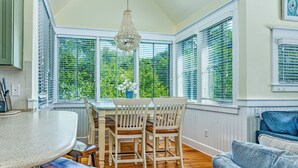 A kitchen with a round island, wooden chairs, and a dining table. - Reverse floor plan cottage with screened in porch. Nature views! (Bald Head Island)