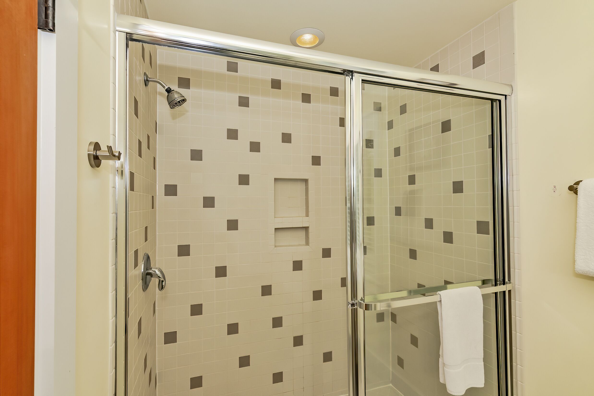 Ducha con cerramiento de vidrio, pared con azulejos y un perchero.