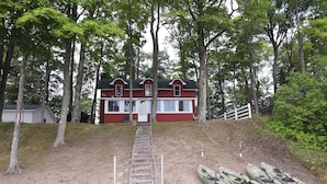 A red building with a staircase leading up to it, surrounded by trees. There are kayaks lined up in front.