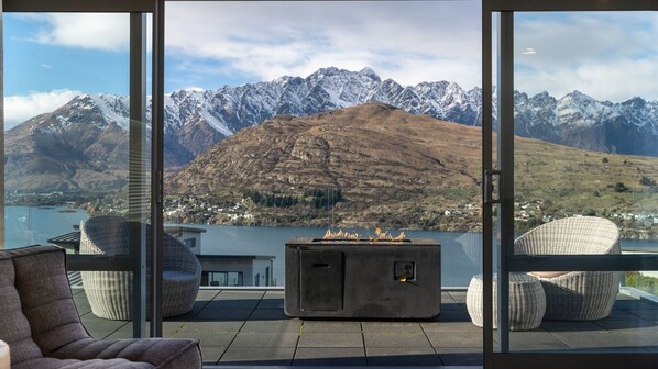 Ein moderner Außenbereich mit Sitzgelegenheit und Kamin, mit Blick auf eine Berglandschaft und einen See.