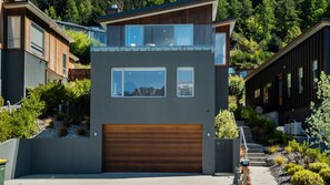 Ein modernes, zweistöckiges Haus mit großer Garage, umgeben von üppiger Vegetation und einer gebirgigen Kulisse.