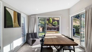 Ein modernes Interieur mit Essbereich, einer Couch und einem großen Fenster mit Blick auf einen Garten und eine Holzterrasse.