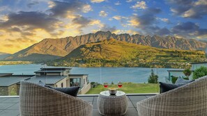 A terrace with wicker furniture overlooking a lake and mountains.