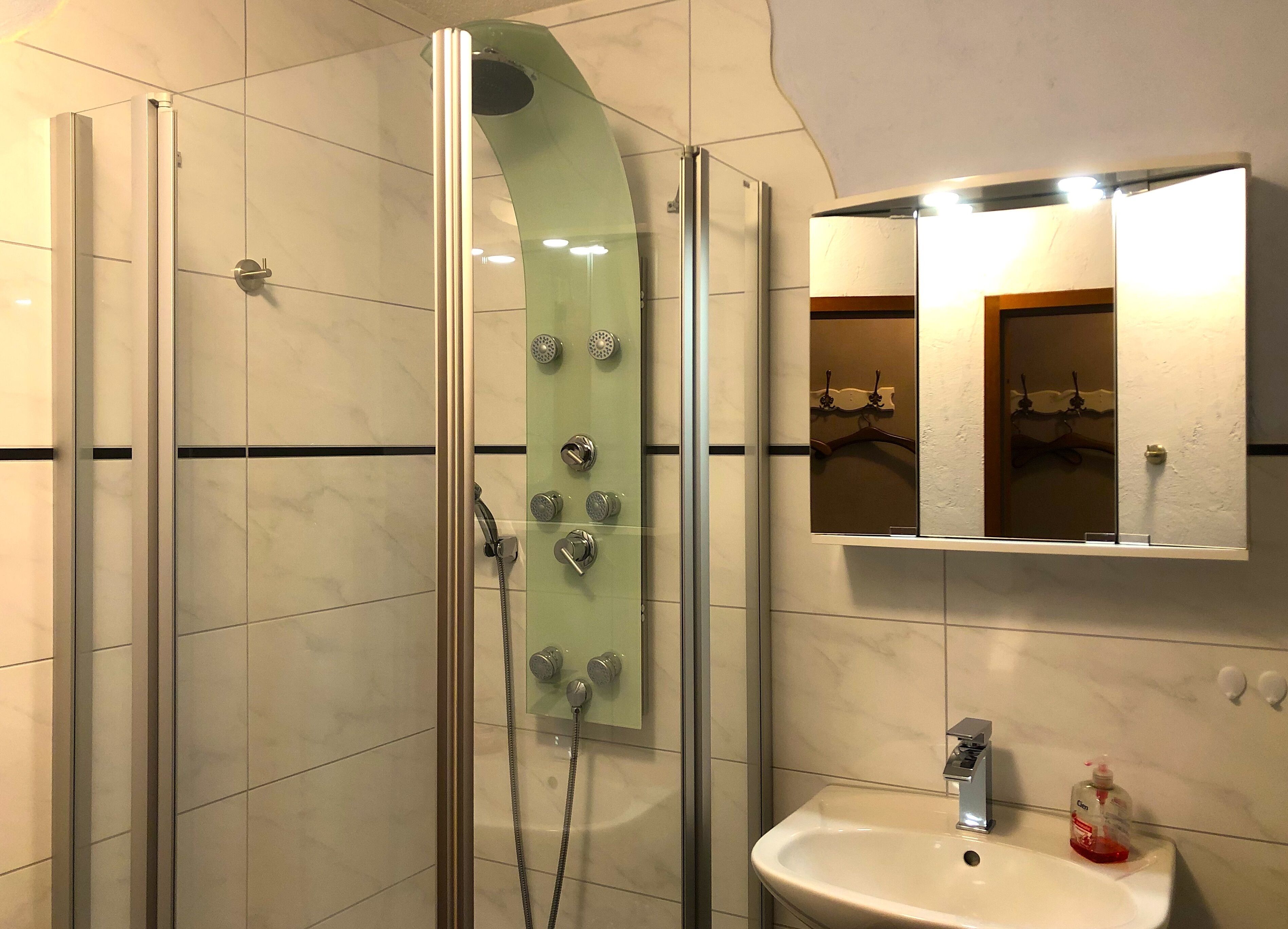 Un bagno moderno con doccia vetrata, lavandino bianco e specchio sopra.