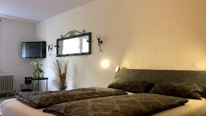 Ett sovrum med en säng, en tv, en spegel och ett litet bord med en växt.